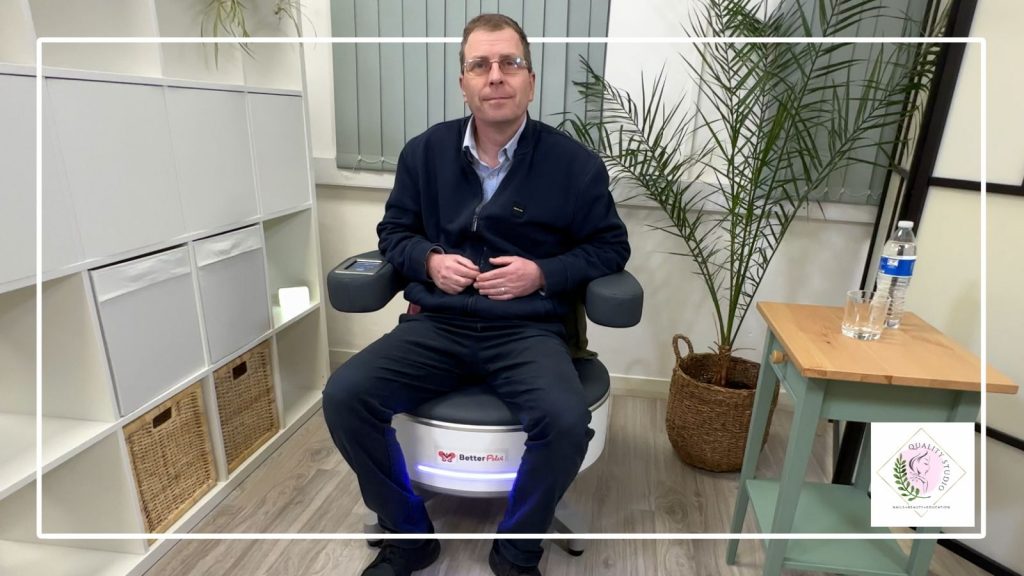 Male client seated fully clothed during a pelvic floor chair trial session in a calm private studio environment.